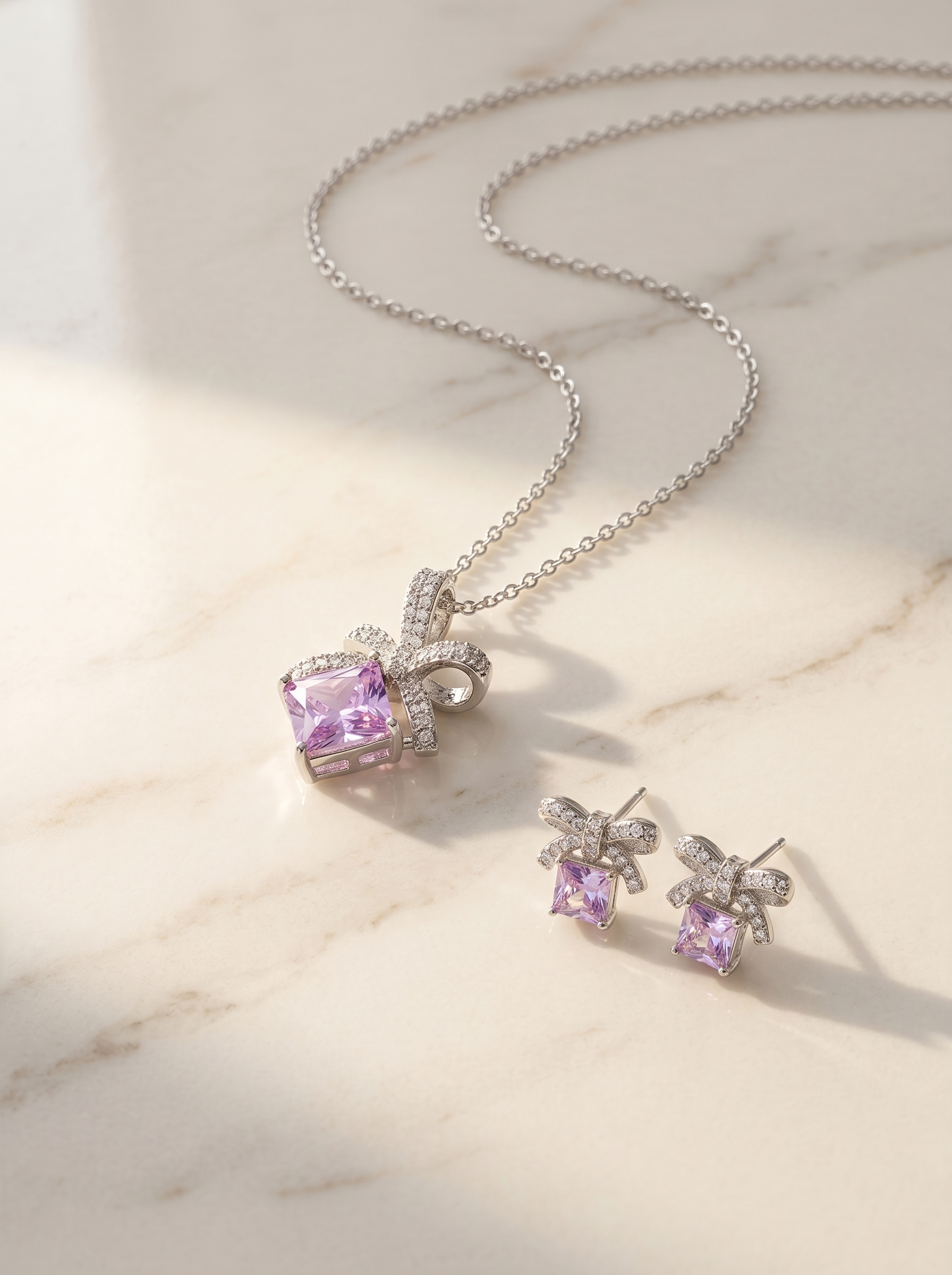 Sterling silver bow ribbon pendant and matching stud earrings laid out on cream marble surface